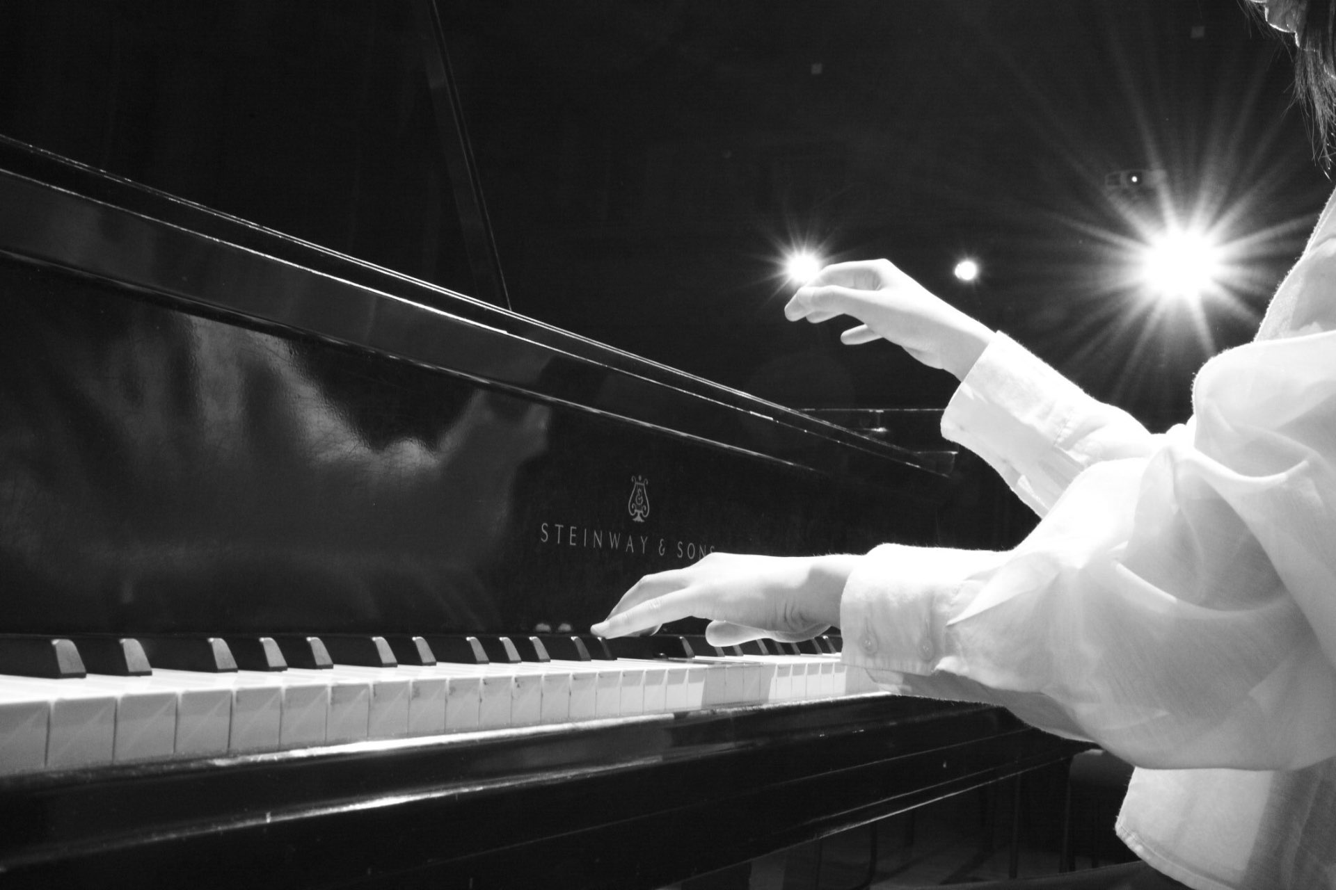 Black and white photo of hands playing a Steinway grand piano on stage